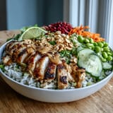 Golden grilled chicken slices rest on fluffy coconut rice beside crisp red cabbage, carrots, cucumber, and creamy peanut sauce.