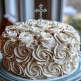 Delicate vanilla sponge cake decorated with silky buttercream, white fondant roses, and a symbolic cross topper.