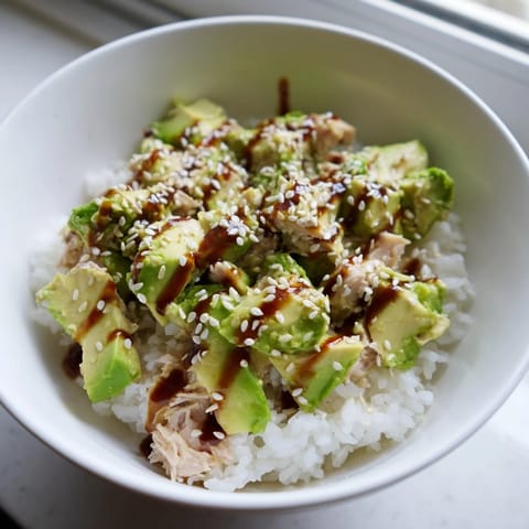 A close-up of the Tuna Avocado Rice Bowl highlights glistening sesame seeds and fresh cilantro over tender tuna and ripe avocado.