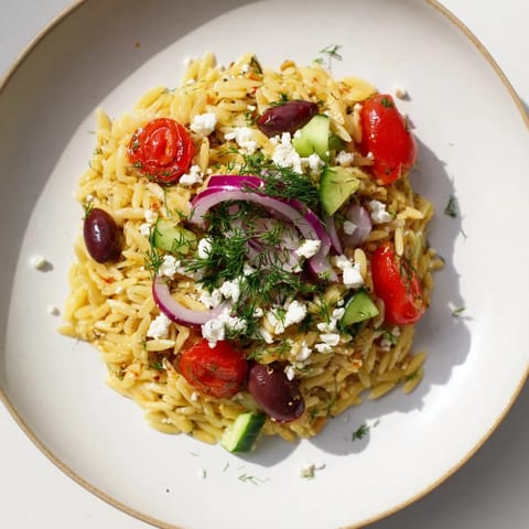A close-up of Greek Orzo Salad with diced cucumber, halved cherry tomatoes, crumbled feta, and fresh parsley on a ceramic plate.