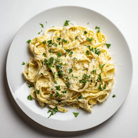 Plated Sriracha Honey Pasta with fettuccine noodles coated in a vibrant orange, creamy sauce next to a wine glass.