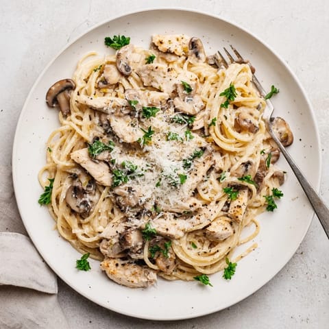 A close-up of Creamy Mushroom Chicken Spaghettini highlights golden seared chicken and silky Parmesan cream sauce clinging to delicate skinny spaghetti.  