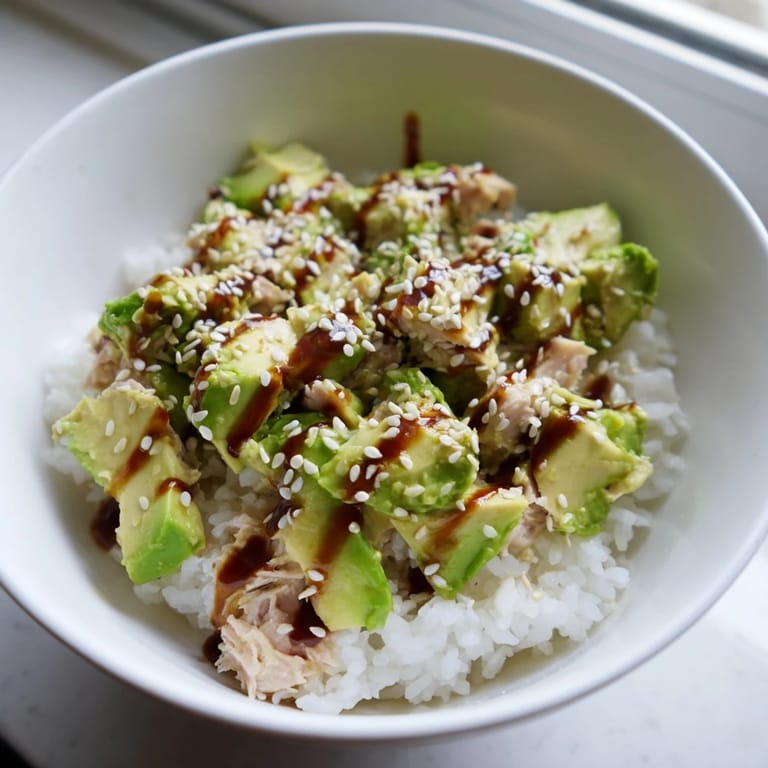 A close-up of the Tuna Avocado Rice Bowl highlights glistening sesame seeds and fresh cilantro over tender tuna and ripe avocado.