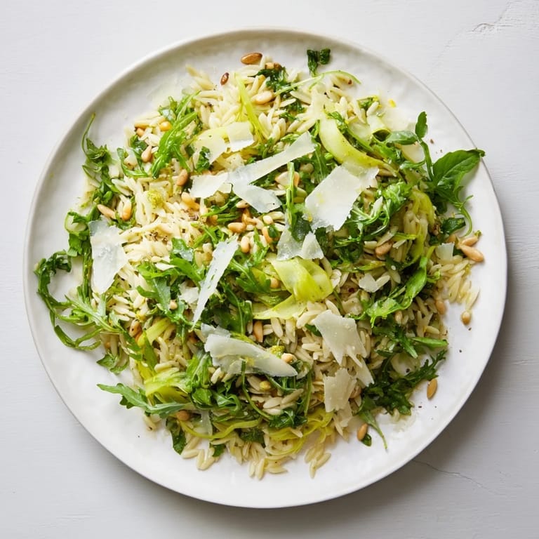 Vibrant Mediterranean orzo and asparagus salad served with extra Parmesan, pine nuts, and lemon wedges on a wooden table.